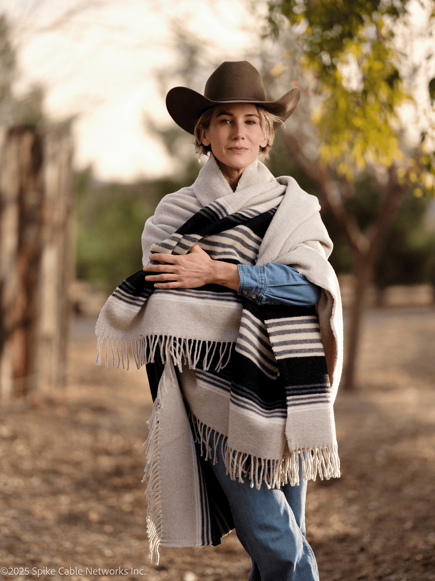 Yellowstone Teeter wearing a cowboy hat and striped shawl in a natural setting