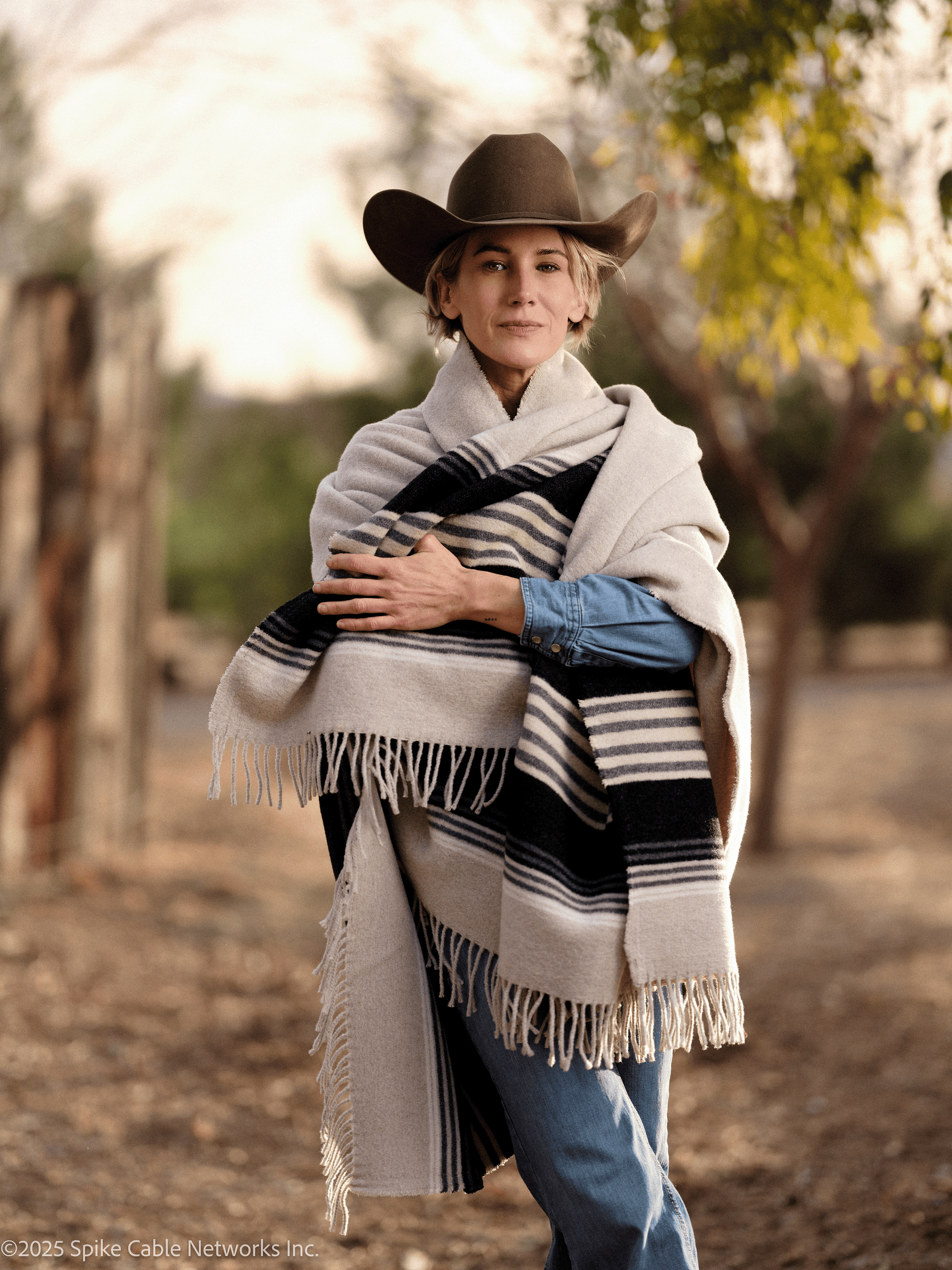Yellowstone Teeter wearing a cowboy hat and striped shawl in a natural setting